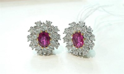 Lot 240 - A pair of ruby and diamond cluster earrings, an oval cut ruby within a border of round...