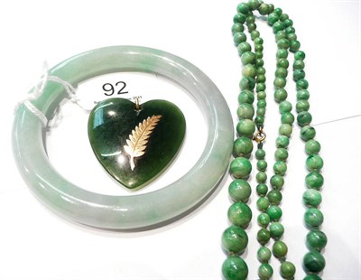 Lot 92 - A jade heart pendant, with fern motif overlaid, a strand of beads and a jade bangle