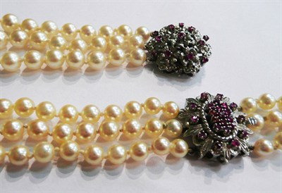 Lot 34 - A three row cultured pearl bracelet, knotted to a ruby set floral design clasp, length 18.5cm and a