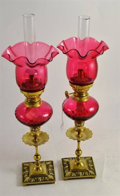 Lot 29 - Pair of brass oil lamps with cranberry shades and reservoirs