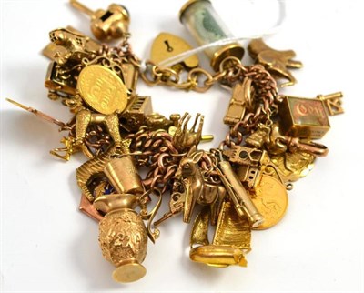 Lot 295 - A 9ct gold charm bracelet hung with approximately thirty gold and yellow metal charms,...