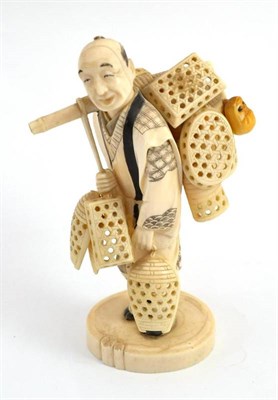 Lot 613 - A Japanese carved elephant ivory figure of a basket vendor, standing smiling, carrying his wares on