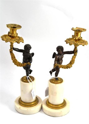 Lot 711 - A pair of parcel gilt bronze figural candlesticks, late 19th century, shaped as a winged putto...