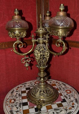 Lot 1381 - A brass three branch oil lamp converted for electricity, height 67cm, by repute housed in...