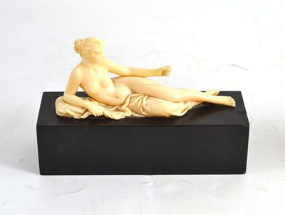 Lot 234 - An ivory figure carved as a nude classical maiden reclining, on a rectangular black marble base...