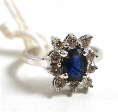 Lot 58 - An 18ct white gold sapphire and diamond cluster ring, the oval cut sapphire within a border of...