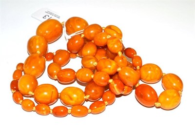 Lot 13 - A string of amber beads, the orangey-yellow graduated barrel shaped beads knotted, without a clasp
