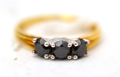 Lot 26 - An 18ct gold three stone black diamond ring, the round cut diamonds in white claw settings on a...