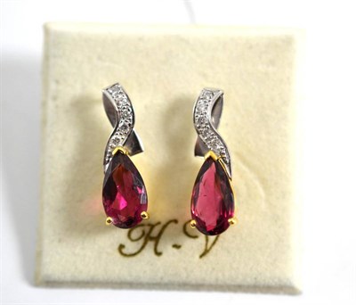 Lot 103 - A pair of tourmaline and diamond earrings, a diamond set swirl over a pear cut purplish-red...