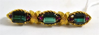 Lot 436 - A tourmaline and ruby brooch, three step cut green tourmaline each within a pair of rubies, in rope