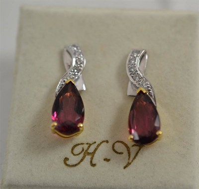 Lot 394 - A pair of tourmaline and diamond earrings, a diamond set swirl over a pear cut purplish-red...