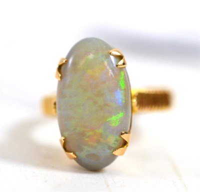 Lot 423 - An opal ring, the oval cabochon opal in a claw setting to linear decorated shoulders on a plain...