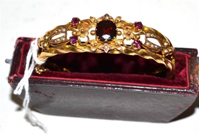 Lot 605 - An early 20th century 9ct gold gemstone set bangle, a garnet centrally, with four pink stones...