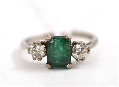 Lot 47 - An 18ct white gold emerald and diamond three stone ring, a step cut emerald flanked by a round...