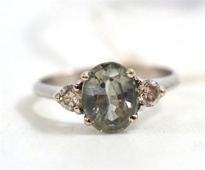 Lot 64 - A green sapphire and diamond ring, the oval cut green sapphire between two round brilliant cut...