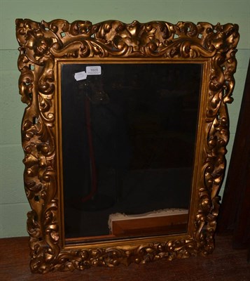 Lot 1605 - A carved giltwood wall mirror with deep scroll border