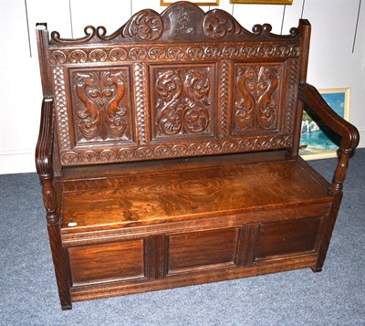 Lot 1645 - A carved oak settle with locker seat and panelled front, carved with an armorial crest