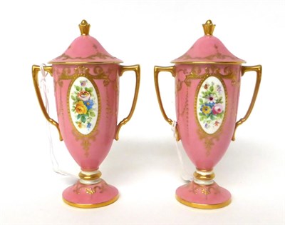 Lot 11 - * A pair of Minton pink ground twin-handled urn shaped vases and covers decorated with flowers,...