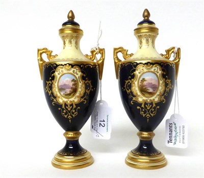 Lot 12 - * A pair of Coalport blue ground twin-handled urn shaped vases and covers, with landscape...