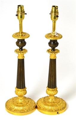 Lot 404 - A pair of parcel gilt bronze candlesticks, the urn shaped sconces over foliate capitals, fluted...