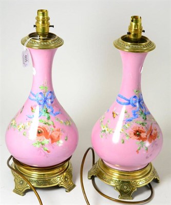 Lot 605 - A pair of late 19th century pink ground and floral decorated table lamps with brass mounts,...