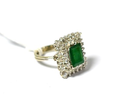 Lot 629 - An emerald and diamond cluster ring, the oblong step cut emerald within a double border of...