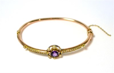 Lot 15 - A 9ct gold amethyst and seed pearl bangle, a round cut amethyst in a yellow milled setting within a