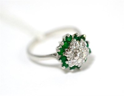Lot 83 - A diamond and emerald cluster ring, a cluster of round brilliant cut diamonds within a border...