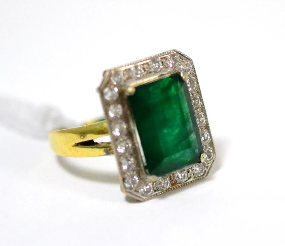 Lot 96 - An emerald and diamond cluster ring, the emerald-cut emerald in a white claw setting, within a...