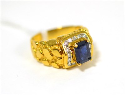Lot 258 - A sapphire and diamond cluster ring, an emerald-cut sapphire in a yellow claw setting, within a...