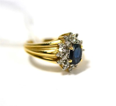 Lot 272 - A sapphire and diamond cluster ring, an oval cut sapphire in a yellow claw setting within a...