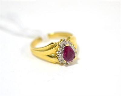 Lot 306 - A ruby and diamond ring, a pear cut ruby in a yellow claw setting within a border of eight-cut...