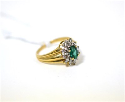 Lot 492 - An emerald ring, an oval cut emerald within a border of round brilliant cut diamonds in yellow claw