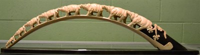 Lot 690 - An early 20th century ivory tusk, carved with elephants with a wooden stand