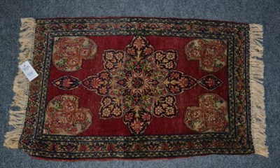 Lot 1242 - A Kirman mat, The plain raspberry field centred by a flowerhead medallion framed by spandrels...