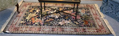 Lot 1282 - A Ghom silk rug, Central Persia, The indigo field of hunting scene enclosed by coral pink cartouche