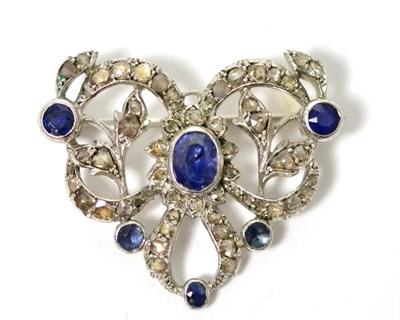 Lot 26 - A sapphire and diamond brooch, an oval cut sapphire in a white rubbed over setting to a ribbon...
