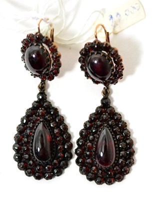 Lot 76 - A pair of garnet drop earrings, an oval cabochon garnet within a border of round cabochon...